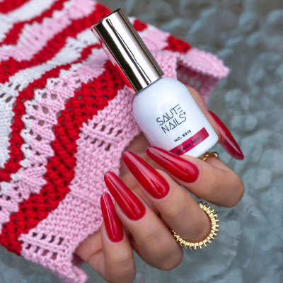 Frasco branco de verniz para unhas SAUTE NAILS Classic Red com unhas vermelhas e fundo de tecido rosa e vermelho