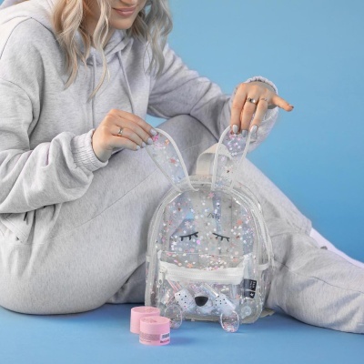 Mochila transparente de plástico com confetes e rosto de coelho, com mulher de fato de treino cinza claro ao fundo