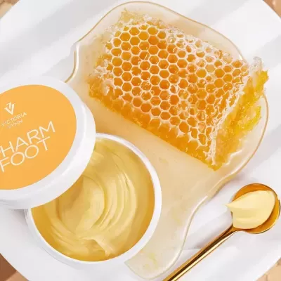 Pote de creme amarelo com favo de mel e colher dourada sobre prato