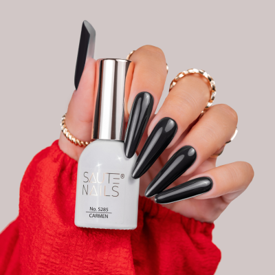 Mão com unhas negras brilhantes segurando verniz de unhas SAUTE NAILS no. 5285 CARMEN