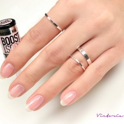 Mão feminina com unhas naturais usando anéis prateados segurando batom Boost