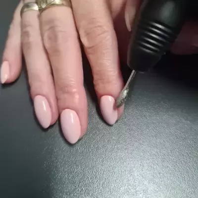 Mão feminina com unhas pintadas rosa claro a ser lixada com ferramenta elétrica preta