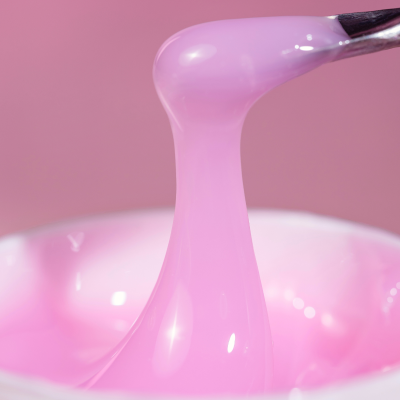 Gel rosa translúcido com textura viscosa e recipiente branco com espátula em fundo rosa
