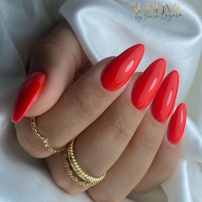 Mão com unhas vermelhas brilhantes e anéis dourados sobre tecido branco