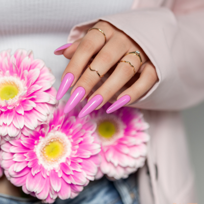 Mãos femininas com unhas rosas vibrantes segurando flores rosa