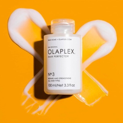 Frasco de OLAPLEX Hair Perfector Nº3 sobre fundo laranja com espuma branca