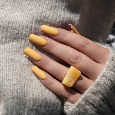 Unhas compridas amarelas com anel quadrado amarelo em fundo bege de camisola de malha