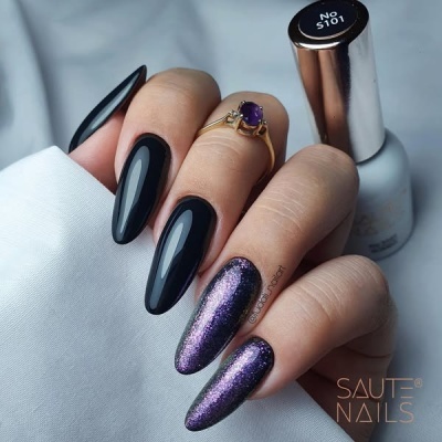 Unhas longas pintadas de preto e roxo metálico com frasco de verniz ao fundo