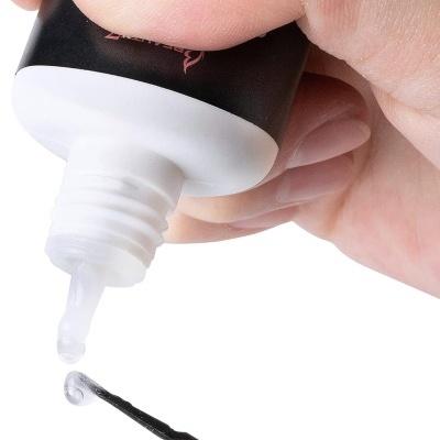 Frasco preto com tampa branca e líquido transparente a sair para uma haste preta.