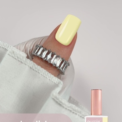 Unha com esmalte gel amarelo pastel e anel prateado com pedras, fundo branco e texto de marca e produto.