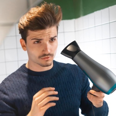 Homem a usar secador de cabelo preto e cinza em ambiente interior com azulejos brancos