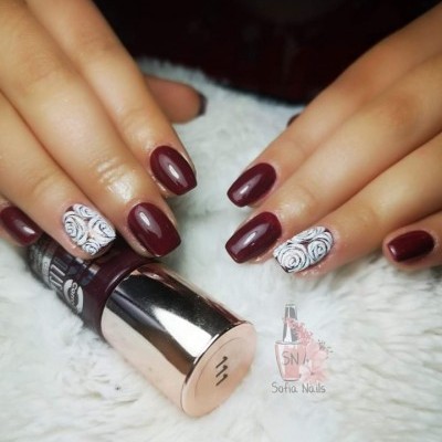 Unhas com verniz vinho e decoração branca com rosas pretas, frasco de verniz e logotipo Sofia Nails