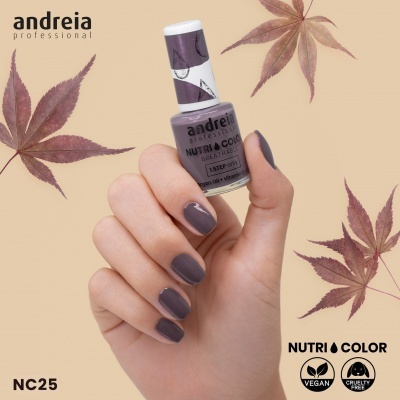 Frasco de verniz Andreia Professional cor NC25 sendo segurado por mão com unhas pintadas da mesma cor, fundo bege e folhas secas