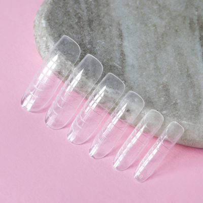 Conjunto de unhas postiças transparentes sobre fundo cinza e rosa.