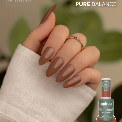 Unhas pintadas de verniz gel castanho nude em mãos femininas com frasco de verniz ao lado e folhas verdes ao fundo