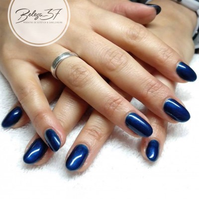 Mãos femininas com unhas azuis metálicas e anel prateado, fundo branco, logótipo Beleza 37