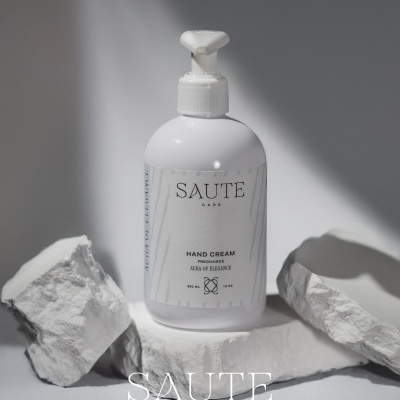 Frasco branco de creme para mãos SAUTE CARE com doseador, sobre pedras brancas