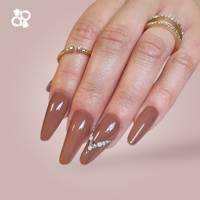 Mãos femininas com unhas compridas castanhas e decoradas com pedrinhas brilhantes