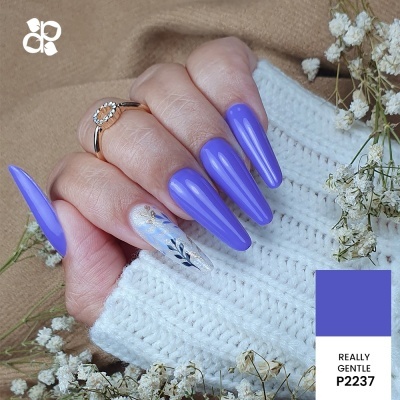 Mão com unhas roxas stiletto e uma decorada, fundo tecido branco de malha e flores secas