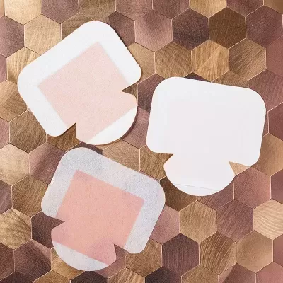 Três curativos adesivos branco e rosa sobre azulejos hexagonais em tons castanhos.