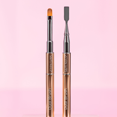 Dois pincéis duplos metálicos dourados para unhas da marca SAUTE NAILS em fundo rosa