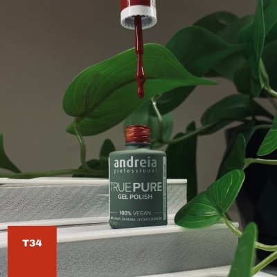 Frasco de verniz gel vermelho andreia professional TRUE PURE sentado sobre superfície branca com planta verde ao fundo