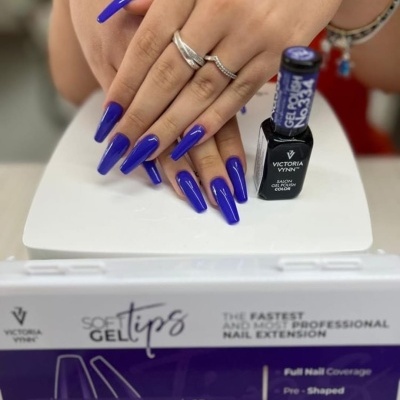 Mãos com unhas compridas pintadas de azul e frasco de verniz Victoria Vynn ao lado