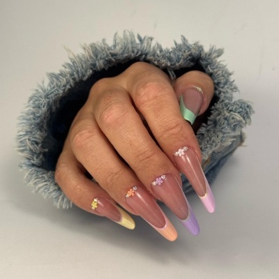 Mão com unhas compridas decoradas em cores pastel e pequenas flores em relevo, vestindo manga de tecido felpudo cinzento