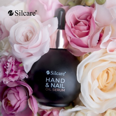 Frasco de óleo para mãos e unhas Silcare rodeado por flores coloridas.