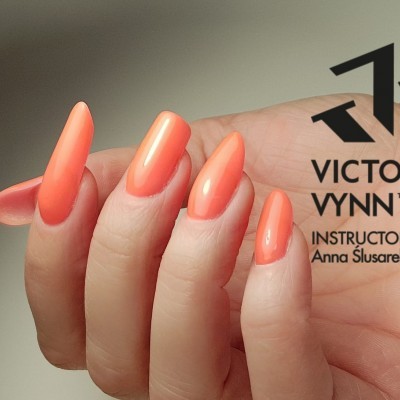 Mão feminina com unhas manicadas em cor coral alaranjada brilhante ao lado do logotipo Victoria Vynn