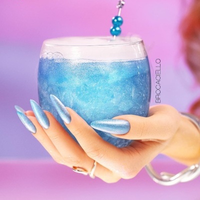 Unhas longas azuis holográficas segurando copo com líquido azul