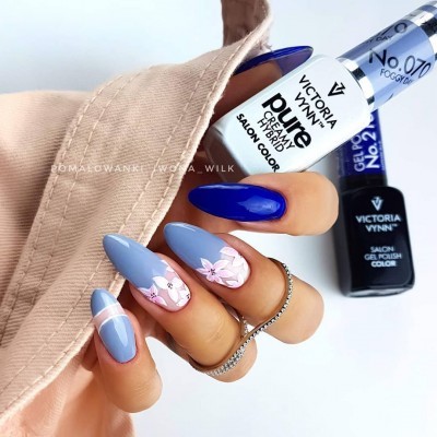 Unhas compridas pintadas com verniz gel azul escuro e azul claro com desenhos florais, mão feminina com anel prateado e manga bege