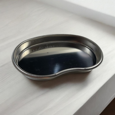 Prato metálico brilhante em forma de rim sobre superfície branca.