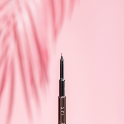 Pincel de unhas fino castanho metálico com sombra de folhas e texto SAUTE NAILS no fundo rosa