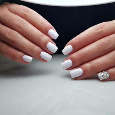 Unhas de gel brancas com uma decorada com pedras brilhantes
