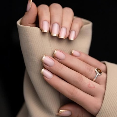 Mãos femininas com unhas nude e ponta dourada, usando anel com pedra âmbar