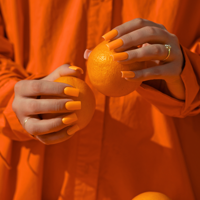Mãos femininas com unhas laranja segurando laranjas sobre fundo laranja com texto SAUTE NAILS®