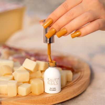 Frasco de verniz para unhas SAUTE NAILS branco e dourado com mão a pintar unha mostarda