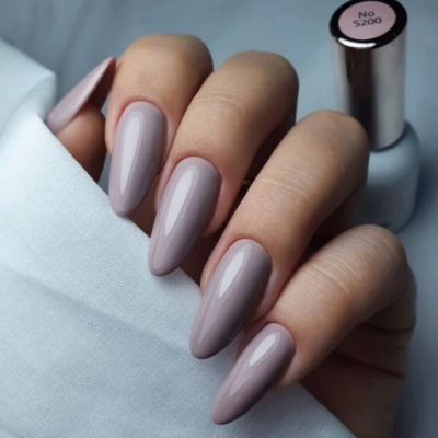Unhas com esmalte cinza rosado brilhante e frasco de esmalte no fundo