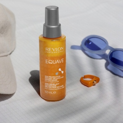 Frasco spray Revlon Professional EQUAVE laranja com chapéu, óculos de sol azuis e anel laranja.