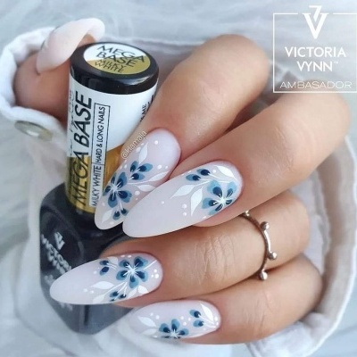 Unhas decoradas com flores azuis segurando verniz WE BASE