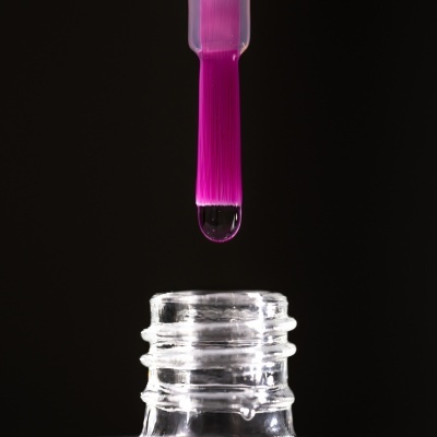 Pincel de unhas cor-de-rosa com gota de líquido sobre frasco transparente