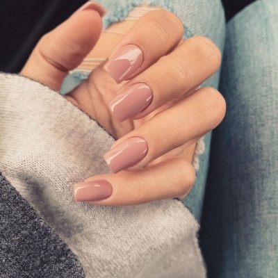 Mão com unhas artificiais cor nude rosa brilhante, fundo de calças de ganga rasgadas