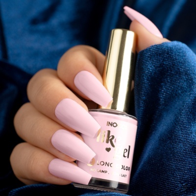 Verniz de unhas rosa claro segurado por mão com unhas da mesma cor sobre tecido azul