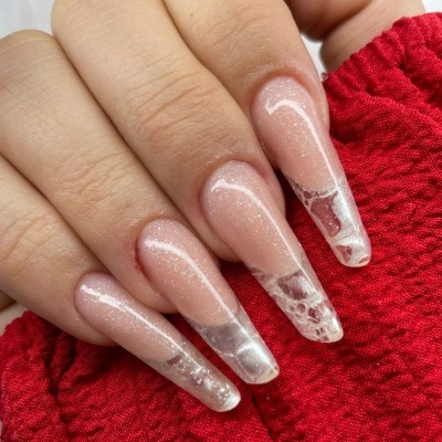 Unhas longas estilo coffin com verniz rosa cintilante e detalhes marmoreados em branco sobre fundo de tecido vermelho.