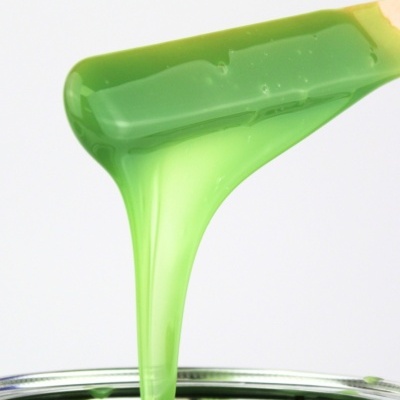 Tinta verde viscosa sendo retirada de lata metálica com espátula de madeira.