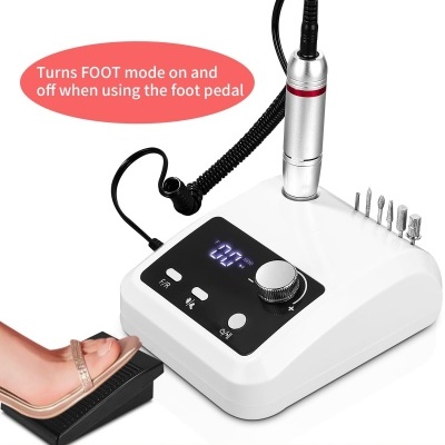 Lixadora para unhas branca com pedaleira preta e brocas metálicas sobre fundo rosa