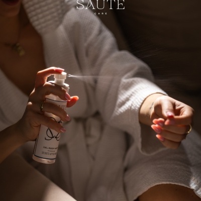 Pessoa a aplicar spray corporal de um frasco branco com bata branca.