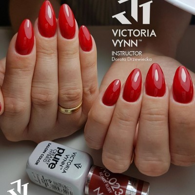 Unhas vermelhas brilhantes com dois frascos de esmalte Victoria Vynn e logotipos na imagem.