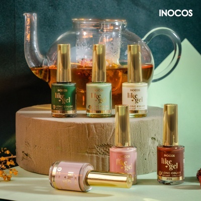 Vernizes para unhas INOCOS like gel em diferentes cores com tampa dourada, dispostos em suporte de madeira com bule de vidro ao fundo.